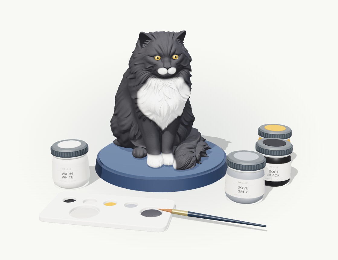 The finished cat figurine: black coat, white bib and paws, amber eyes, with four pots of acrylic paint, a palette and a brush beside it