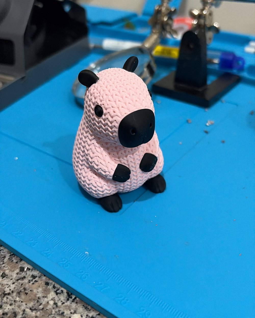 A pink capybara printed with a knitted-wool texture, on a workbench