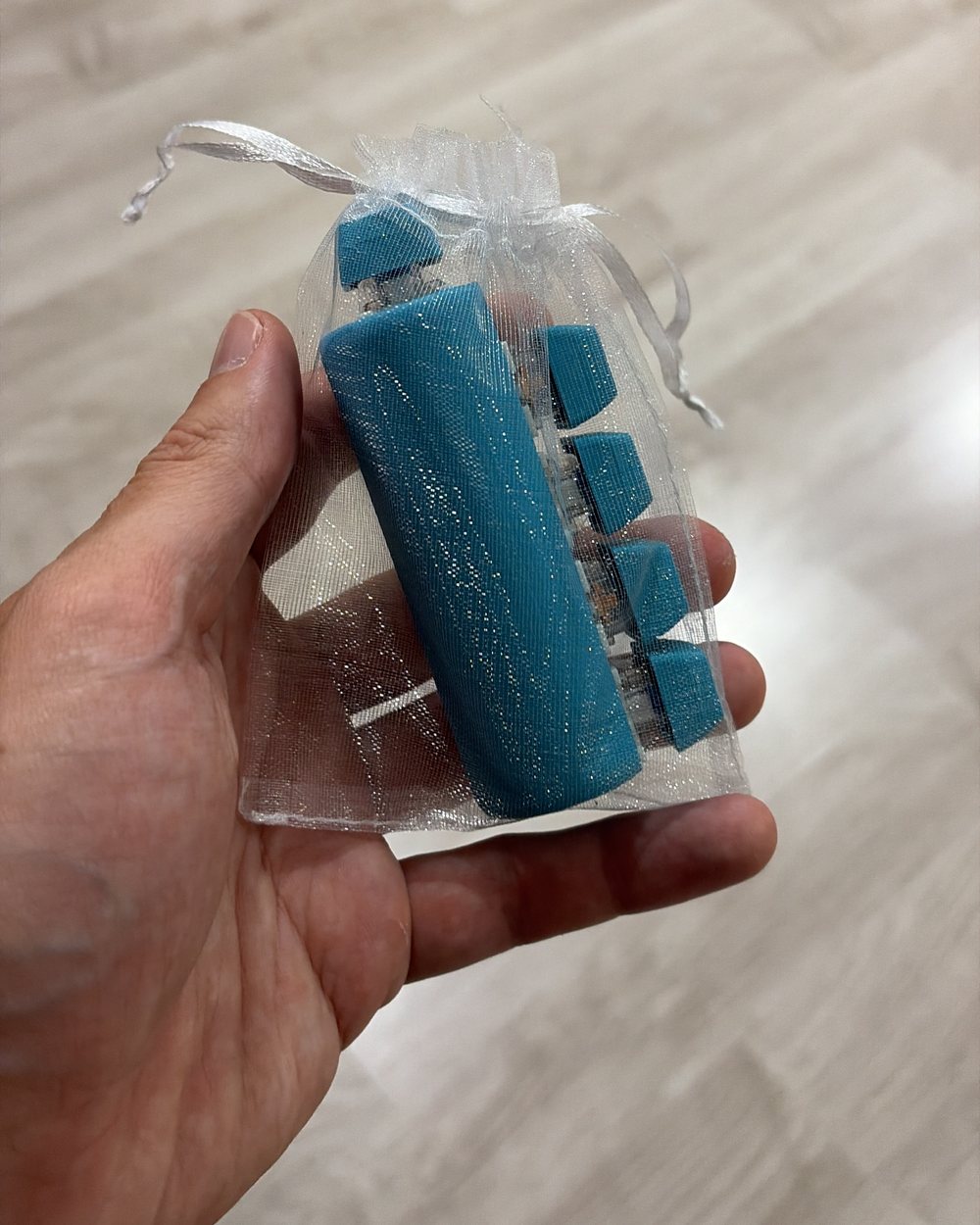 A teal five-finger fidget clicker in an organza gift bag, held in a hand