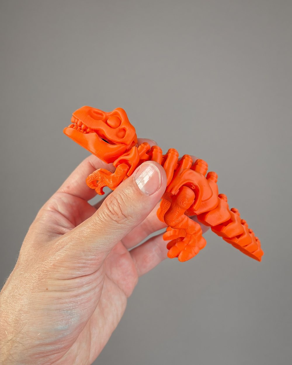 A bright orange articulated T-rex held between someone's fingers