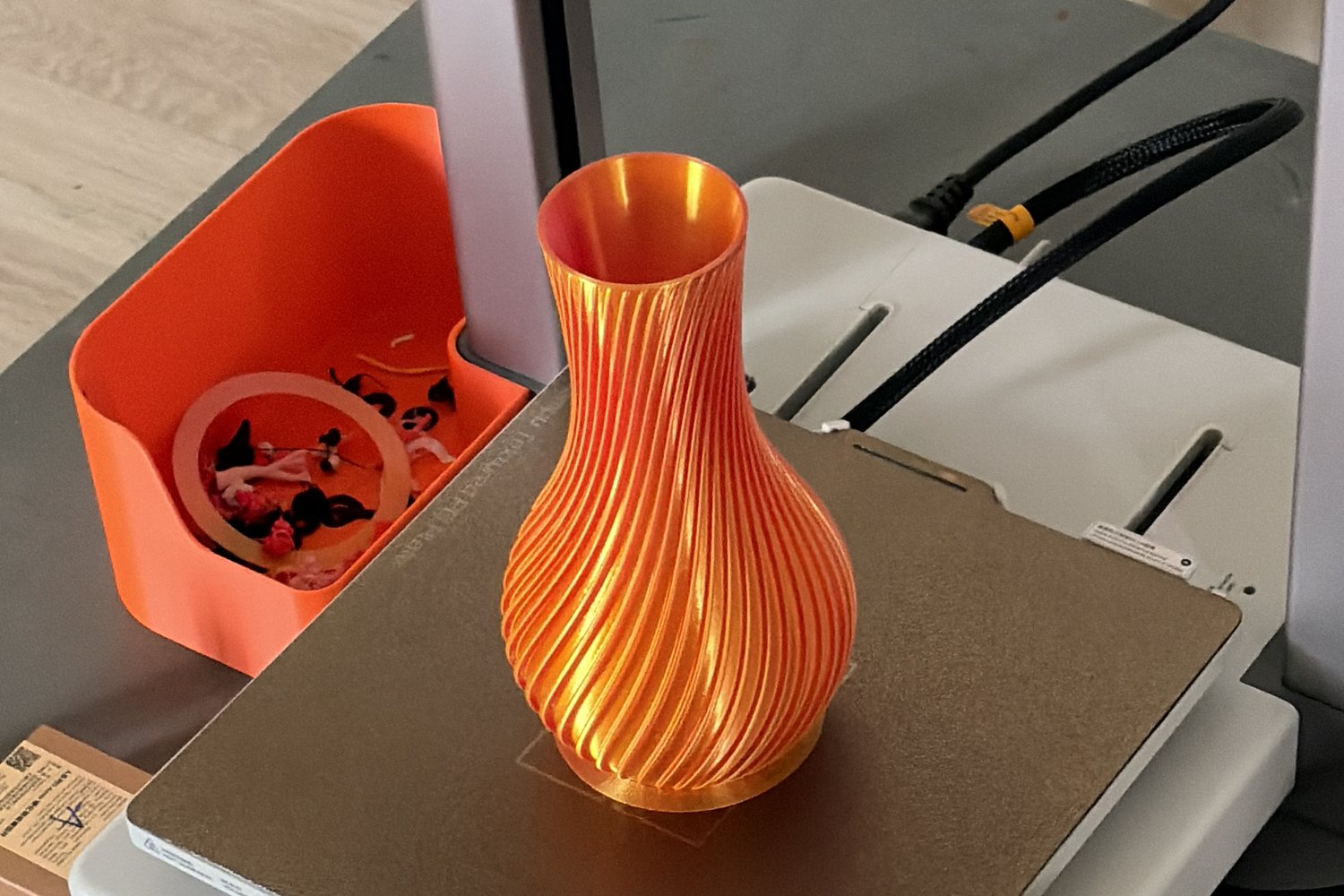 An orange spiral vase, just finished, standing on the build plate of the Bambu Lab A1 printer at home