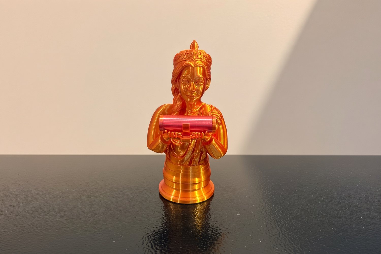 The queen reprinted in gold and pink, holding a scroll tube in both hands, on a dark table